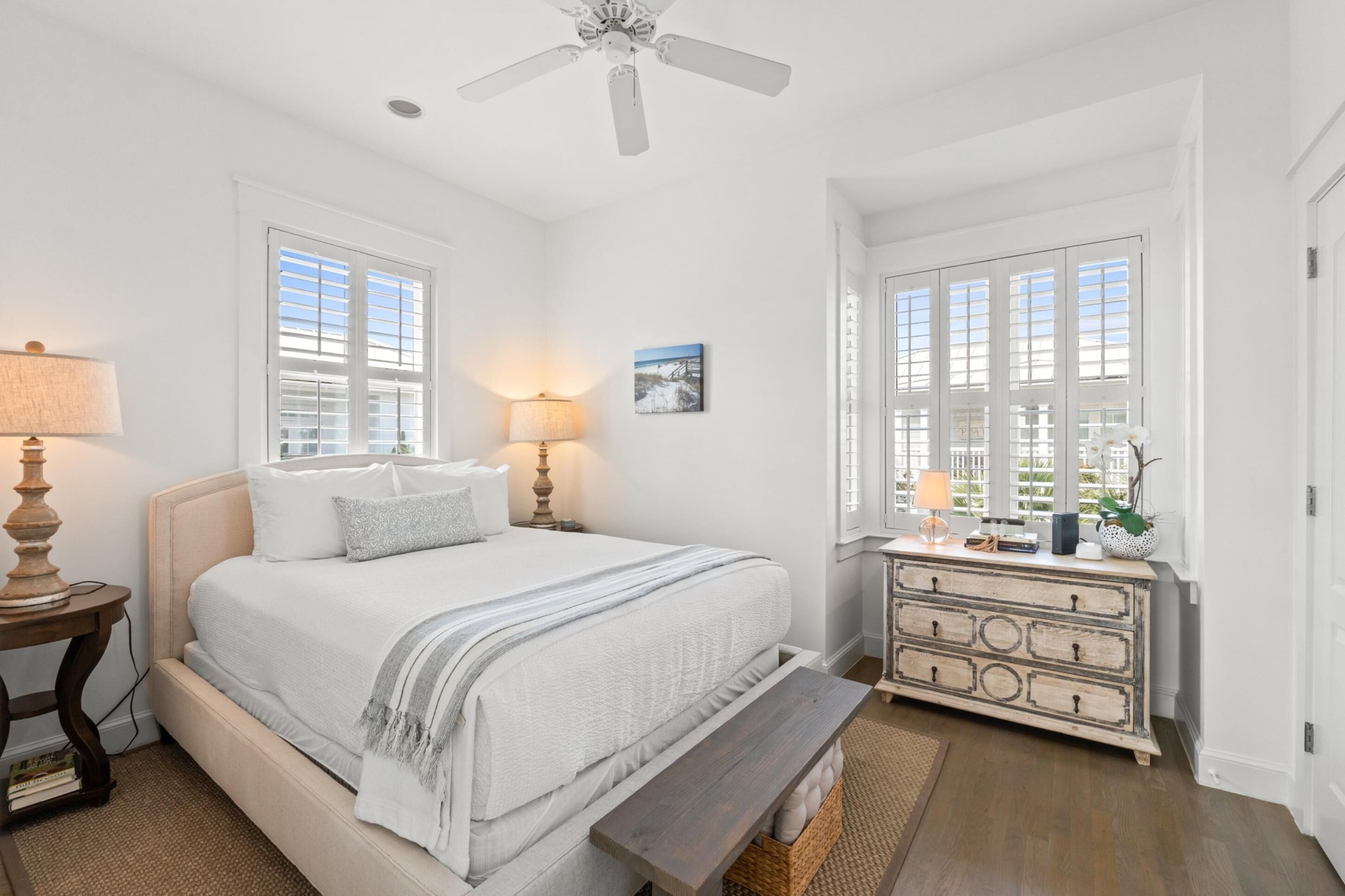 Une chambre à coucher comprenant un lit, des tables de chevet, une commode et un ventilateur de plafond.