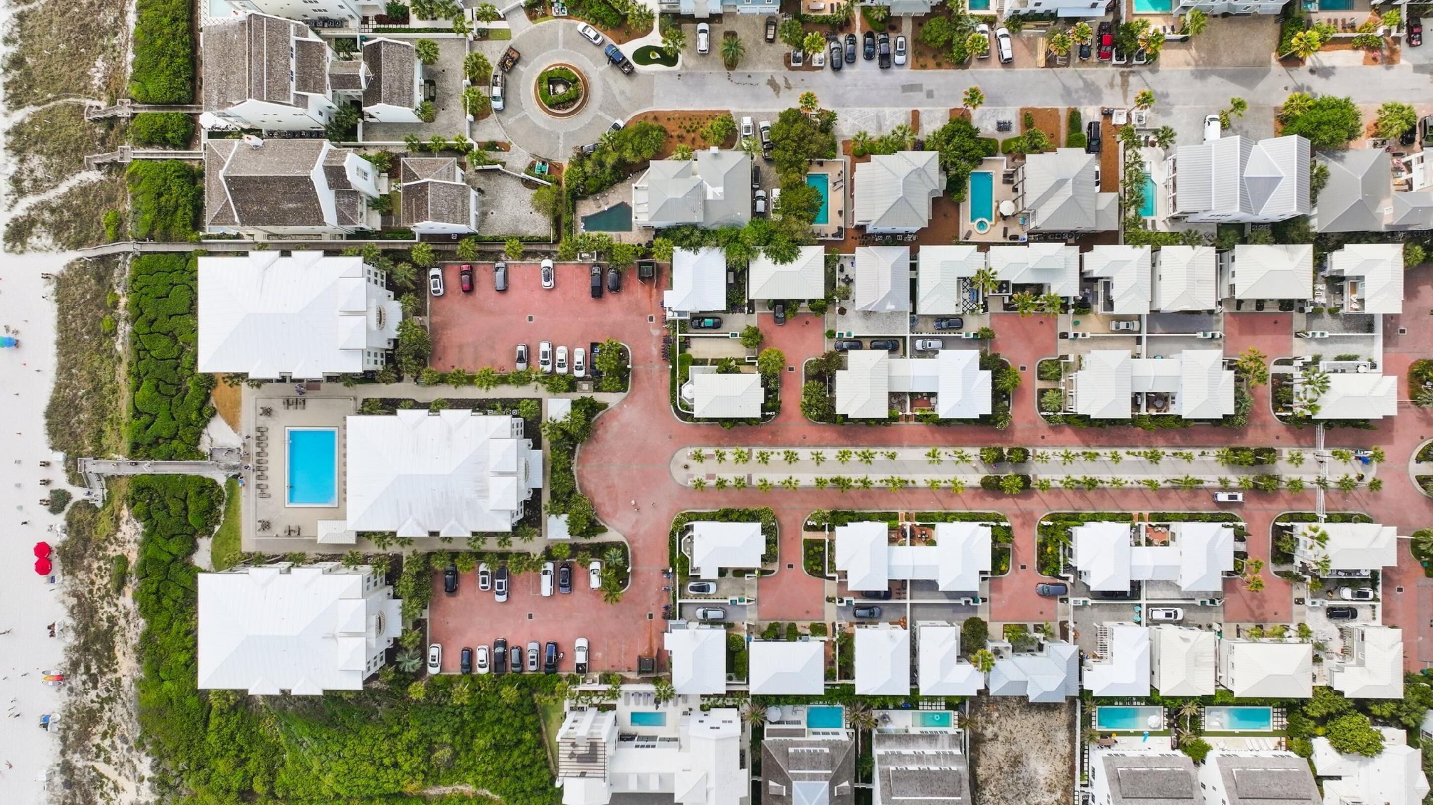 Vue aérienne d’un complexe hôtelier comprenant plusieurs bâtiments, une piscine centrale et une zone de plage.