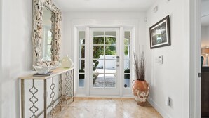 A hallway with a white door, a decorative mirror, a console table, and a large potted plant. - 30A Sunset Beach House - Villa Infinity (Panama City Beach)