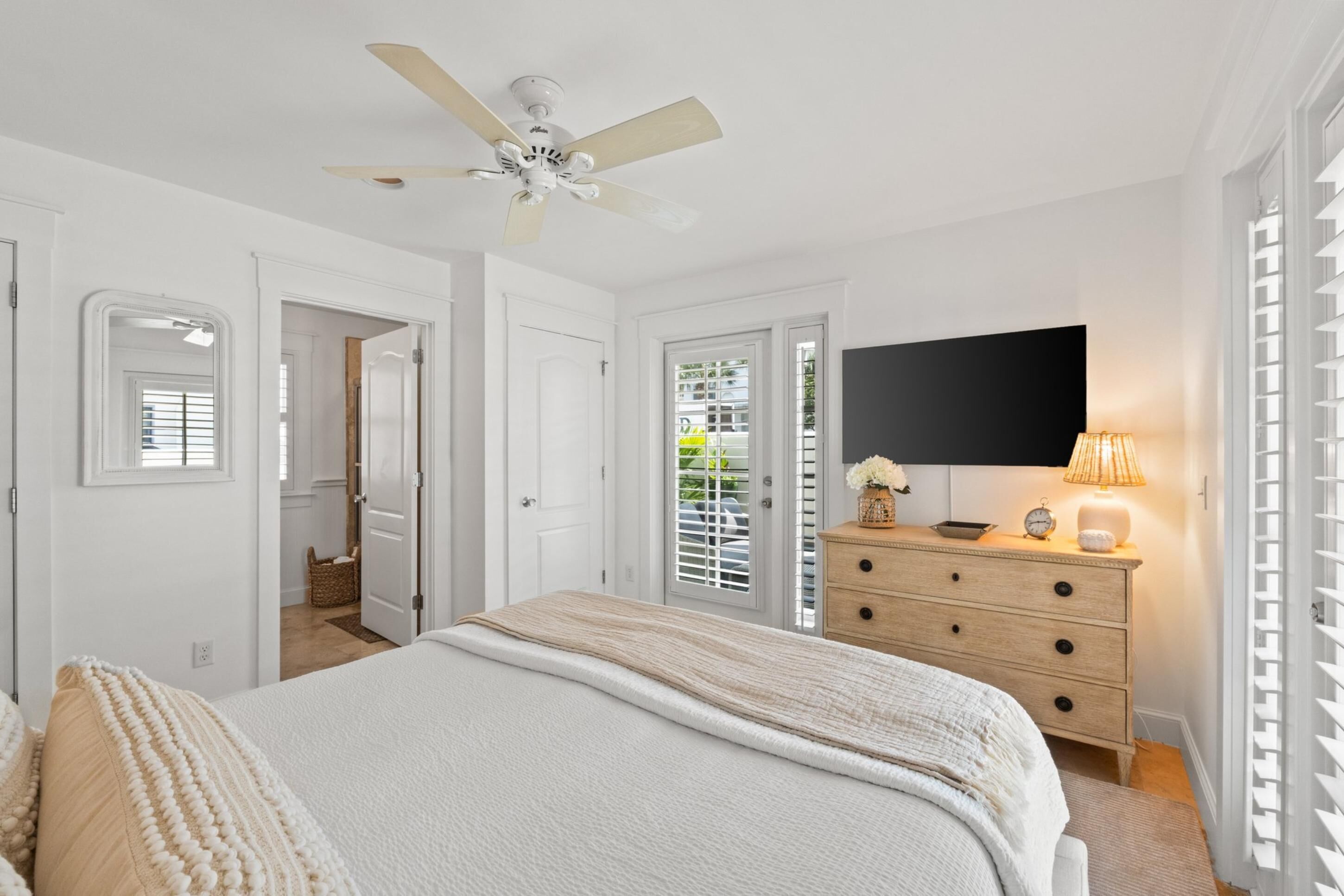 Une chambre à coucher avec un lit, une commode, un ventilateur de plafond et un téléviseur.