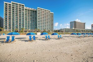 Ein Strandhotel mit mehreren Etagen, Liegestühlen und Sonnenschirmen.