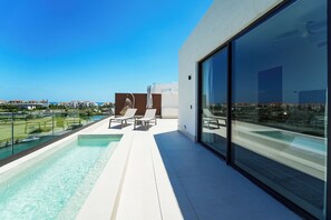 A modern outdoor pool area with clear blue water, a glass-enclosed balcony, and a view of the surrounding landscape.
