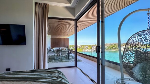 Una habitación de hotel moderna con una cama grande, televisor y balcón con una silla colgante y vista al mar.