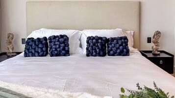 A neatly made bed with a white headboard, two large decorative pillows, and a white throw blanket.