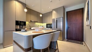 Cocina moderna con una isla central, taburetes de bar, electrodomésticos de acero inoxidable e iluminación colgante.