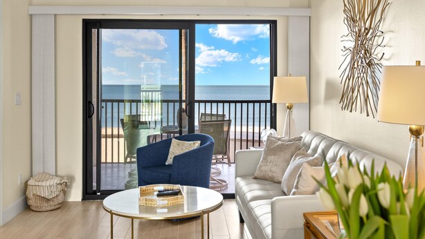 Una sala de estar con balcón con vista al mar, un sofá, una mesa de centro y una lámpara.