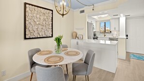 Una cocina moderna con armarios blancos, un refrigerador de acero inoxidable y una ventana con vista a palmeras.