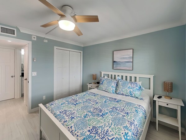 A bedroom with a bed, a ceiling fan, a nightstand, a wall-mounted lamp, and a door.