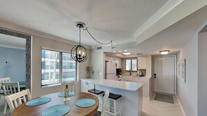 A modern kitchen with white cabinets, a central island, and a dining area with a wooden table and white chairs.