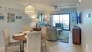 Ein Essbereich mit Korbstühlen und einem runden Tisch, ein Wohnzimmer mit einer Couch und Sesseln sowie ein Balkon mit Blick.