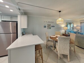 A modern kitchen with a built-in island, stainless steel refrigerator, and wicker chairs around a wooden dining table.