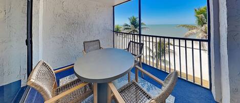 Un balcon avec une table ronde et quatre chaises en osier, donnant sur une plage.