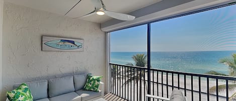 A balcony with a view of the ocean, a ceiling fan, a sofa with cushions, and a sign on the wall.