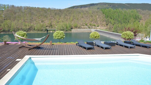 A pool area with lounge chairs and a hammock, overlooking a lake and forested hills. - Villa in Stavelot With Lake View and Jacuzzi (Stavelot)
