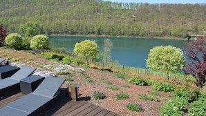 A lakeside deck with lounge chairs, a wooden deck, and a view of a lake surrounded by trees. - Villa in Stavelot With Lake View and Jacuzzi (Stavelot)