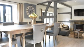A dining area with a wooden table and chairs, a clock on the wall, and a fireplace in the background. - Villa in Stavelot With Lake View and Jacuzzi (Stavelot)