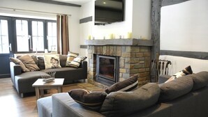 A modern living room with a stone fireplace, grey sofas, and a flat-screen TV mounted above the fireplace. - Villa in Stavelot With Lake View and Jacuzzi (Stavelot)