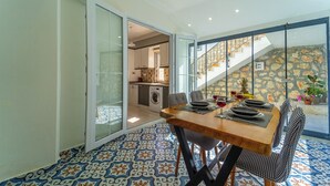 Un comedor con mesa de madera y sillas a cuadros, una cocina al fondo y una escalera que lleva a un nivel superior.