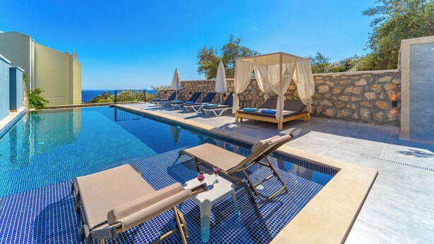 Un área junto a la piscina con sillones, una mesa con bebidas y vistas al mar.