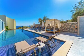 Área da piscina com espreguiçadeiras, uma mesa com bebidas e vista para o mar.