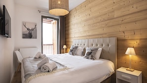 Une chambre à coucher avec un grand lit, une tête de lit en bois, une table de chevet avec une lampe et un téléviseur fixé au mur.