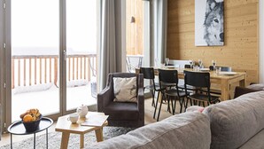 Un salon confortable avec un canapé, une table basse et une table à manger avec des chaises. Il y a un balcon avec une balustrade en bois et une vue sur l’extérieur.