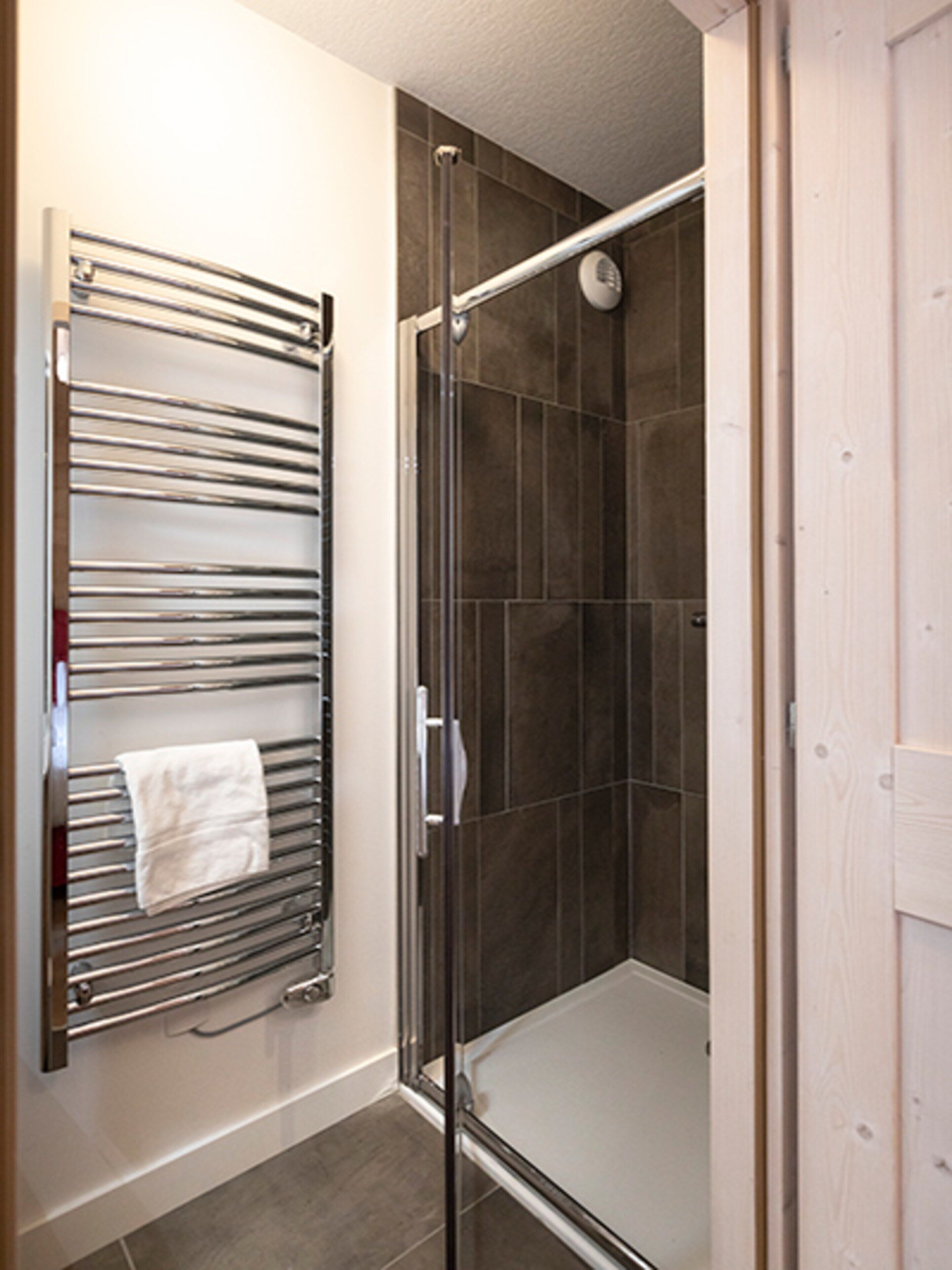 A shower area with a glass door, a towel rack with a towel, and tiled walls.