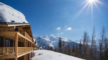 A wooden chalet with a balcony overlooking a snowy mountain landscape.