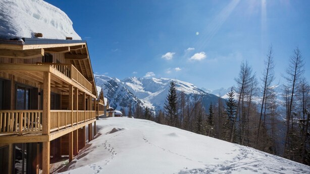 Un chalet en bois doté d’un balcon donnant sur un paysage montagneux enneigé.