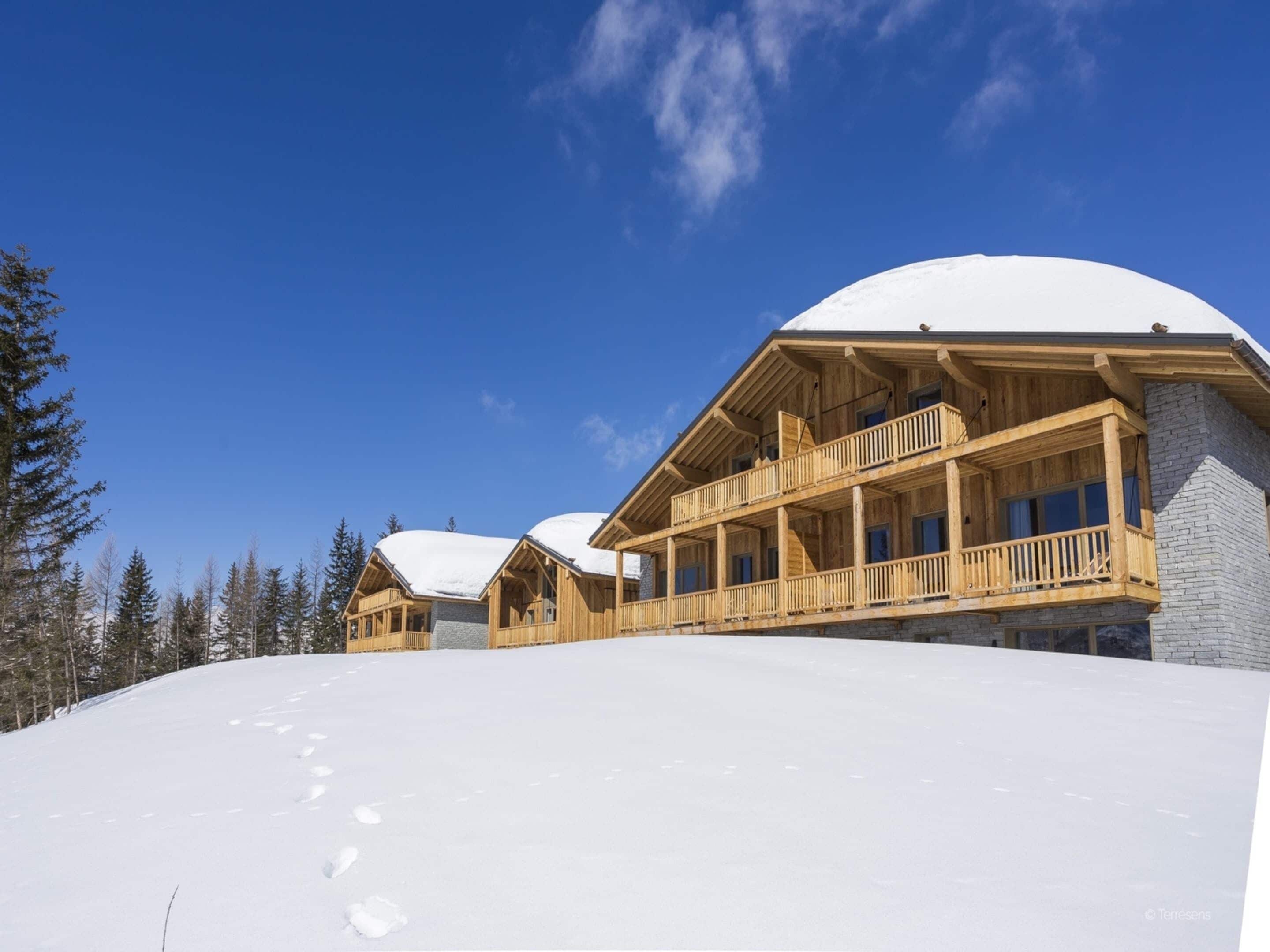 A wooden lodge with a snow-covered roof, wooden balconies, and a clear blue sky.