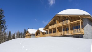 Un chalet en bois, avec un toit enneigé, des balcons en bois et un ciel d’un bleu éclatant.