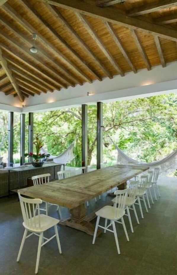 Enjoy meals in this spacious dining area with a long table and comfortable seating, surrounded by natural beauty.