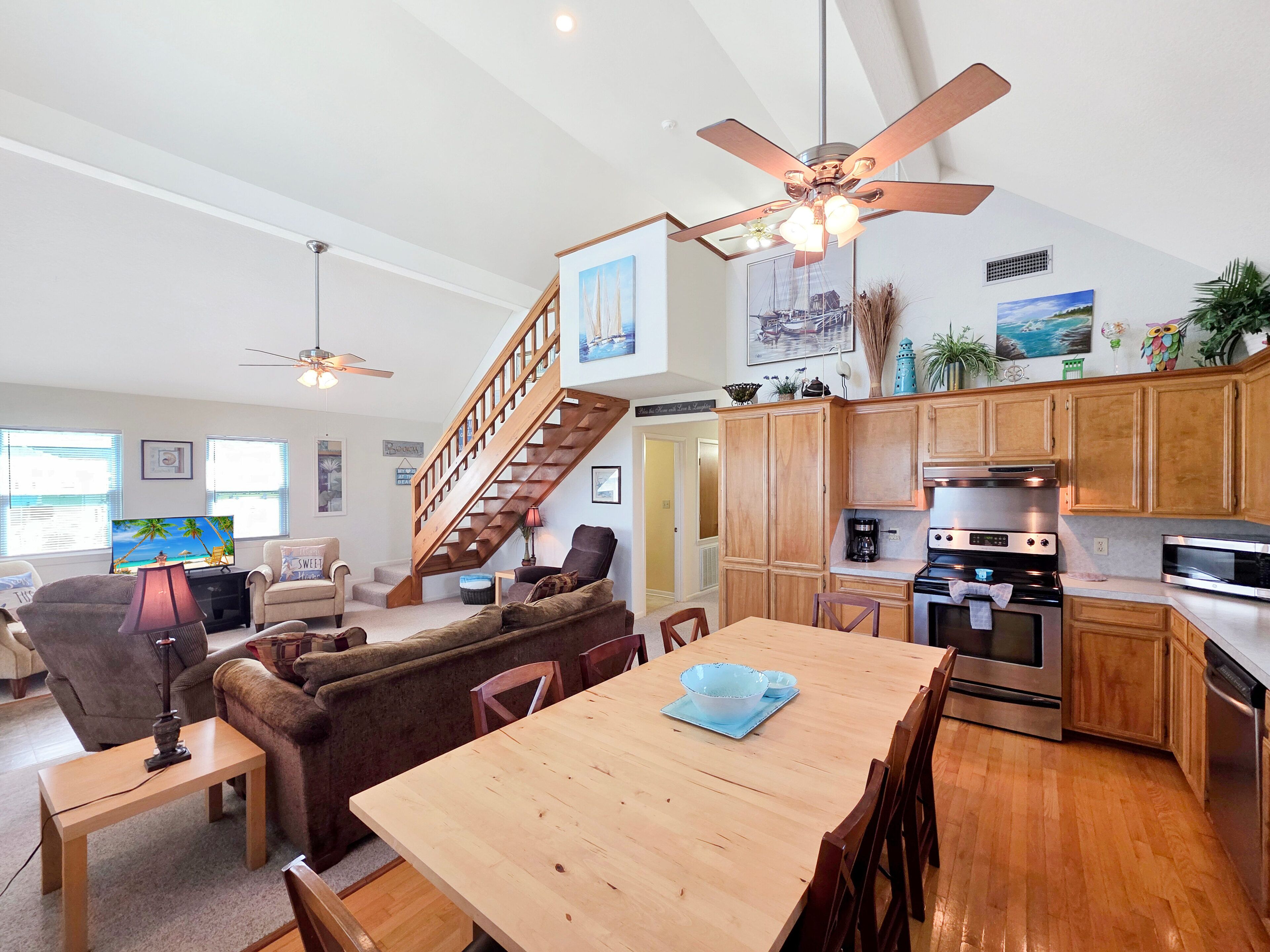 A spacious living area with a wooden dining table, comfortable seating, a kitchen with modern appliances, and a staircase leading to an upper level.