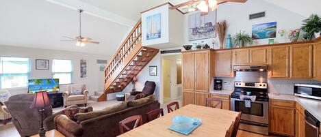 A spacious living area with a wooden dining table, comfortable seating, a kitchen with modern appliances, and a staircase leading to an upper level.