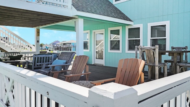 A covered deck with wooden chairs and tables, a light blue building with white trim, and a view of other buildings in the background.