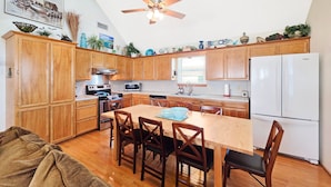 A kitchen with wooden cabinets, a dining table with chairs, a ceiling fan, and a refrigerator.