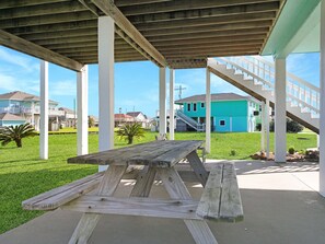 Ein überdachter Außenbereich mit Picknicktisch, weißen Säulen und einer Treppe, die zu einem türkisfarbenen Haus führt.