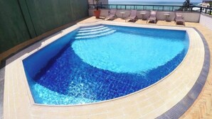 A swimming pool with a curved edge, surrounded by lounge chairs and a view of the ocean.