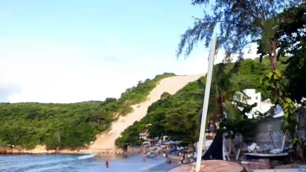 A beach scene with a person holding a green coconut with a straw. - NATAL PLAZA - Suite on the 19th floor (Vila de Ponta Negra Natal)