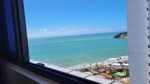 A coastal view from a window overlooking a beach with buildings and a clear sky. - NATAL PLAZA - Suite on the 19th floor (Vila de Ponta Negra Natal)