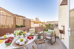An outdoor dining area with a table set for two, surrounded by wicker chairs and a small side table with a vase of flowers. - Modern Elegance inside Lucca Walls – with Terrace (Lucca)