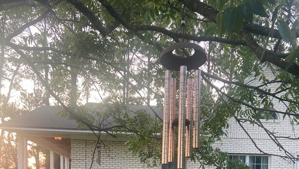 Une maison avec une façade en briques, un porche doté d’une balustrade et un carillon éolien suspendu.
