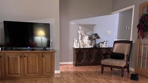 Un salon avec un plancher en bois, un téléviseur, un meuble et un fauteuil.