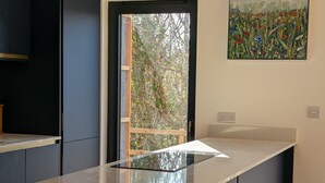 Uma cozinha moderna com uma ilha central, dois banquetes altos e um quadro na parede.