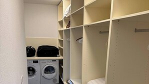 A laundry room with a washing machine and dryer, a bed with a white mattress, and a shelf with shoes. - Charming Austrian Home Near Hallstatt - Perfect Base for Your Salzburg Getaway (Attnang-Puchheim)