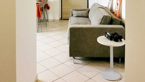 Un espacio habitable compacto con un sofá, una mesita redonda y una zona de comedor con sillas.