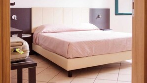 Un dormitorio con cama, mesita de noche, lámpara y un pequeño escritorio con silla.