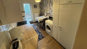 Een compacte keuken met een wasmachine, een koelkast, een magnetron en een eethoek met een tafel en stoelen.