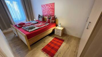 A neatly arranged bedroom with a wooden bed, a red blanket, and a small bedside table with a lamp.