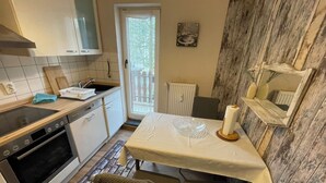 Een kleine keuken met een kookplaat, oven en spoelbak. Er is een eettafel met stoelen en een raam met uitzicht.